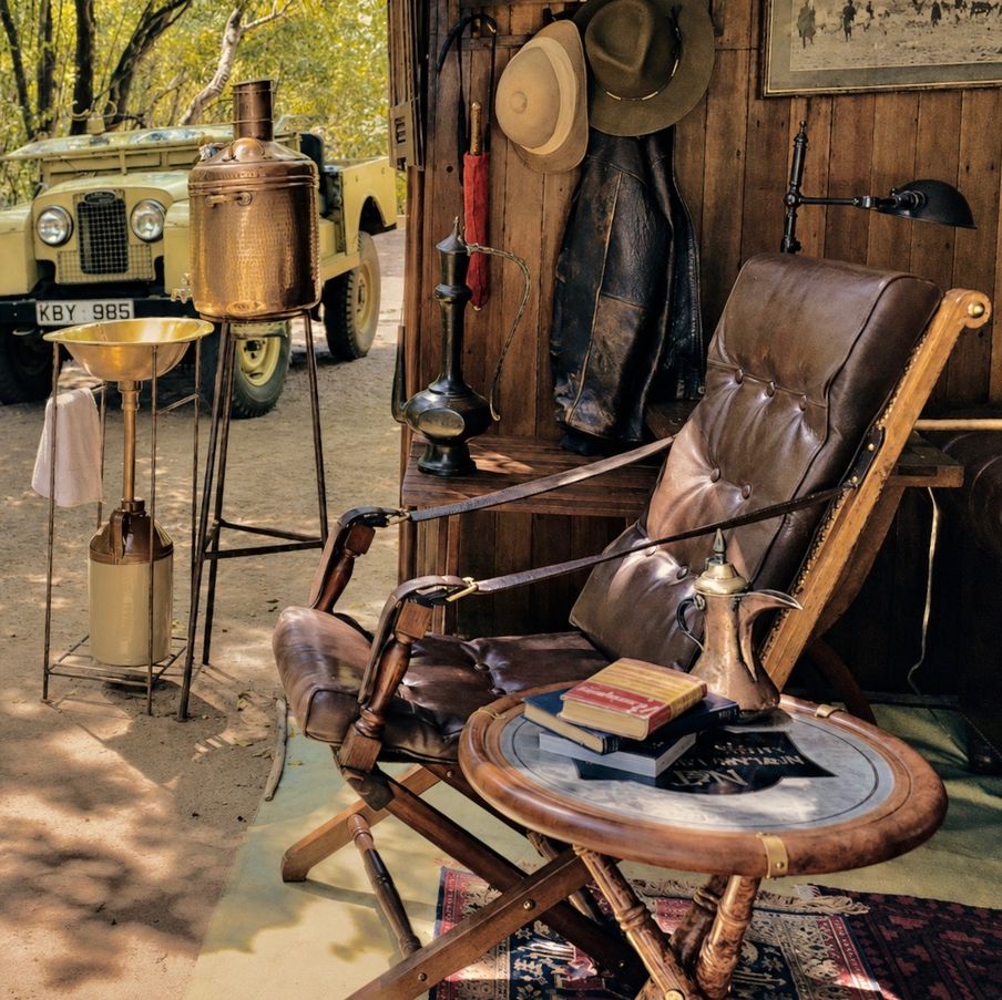 A leather campaign chair and folding table beside a canvas washstand and a Land Rover