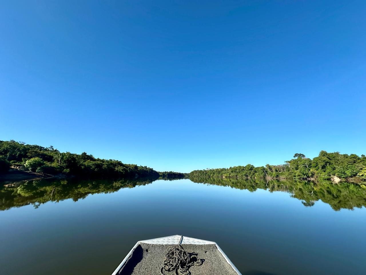 The bow of a boat on flat water at first light, forest on both banks